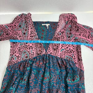 Op de afbeelding: Een jurk met lange mouwen met een V-hals en een paisley patroon in roze en teal. De jurk heeft een borstbreedte van ongeveer 53 cm. De jurk heeft een relaxte pasvorm en een bohemien stijl.