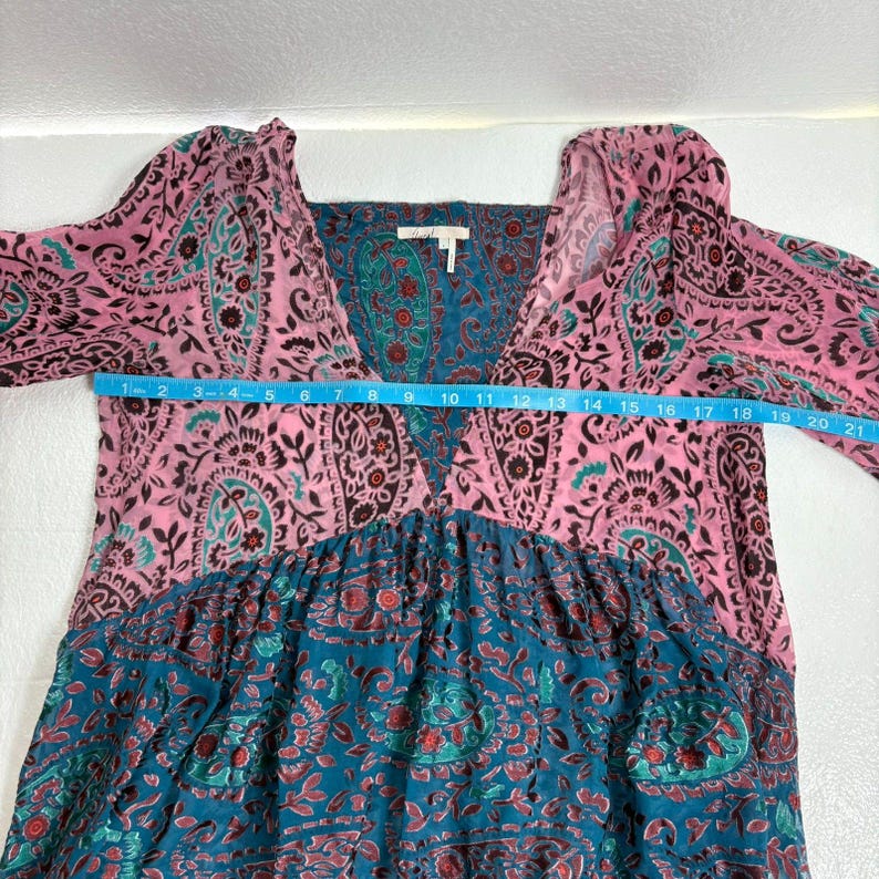 Op de afbeelding: Een jurk met lange mouwen met een V-hals en een paisley patroon in roze en teal. De jurk heeft een borstbreedte van ongeveer 53 cm. De jurk heeft een relaxte pasvorm en een bohemien stijl.