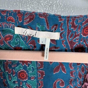 Op de afbeelding: Close-up van een teal top met een paisley patroon in bordeaux, teal en groen. Het label leest "Aireat" en "Made in China". De top is maat small.