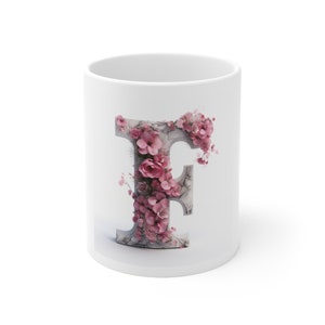 May include: White ceramic mug with a pink floral design in the shape of the letter F.