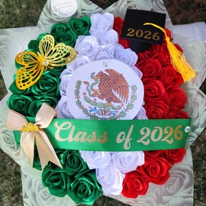Op de afbeelding: Een afstudeerboeket in de kleuren van de Mexicaanse vlag, met groene, witte en rode rozen. Het bevat een gouden vlinder, een lint met "Class of 2026" en een afstudeerhoed. Het boeket is een feestelijk arrangement.