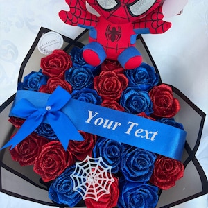 May include: A bouquet of red and blue roses with a blue ribbon that reads "Your Text". A Spider-Man plush toy sits atop the arrangement. A white spiderweb decoration is also included.