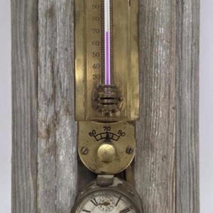 May include: A wall-mounted instrument featuring a brass thermometer labeled The Minneapolis with a purple liquid column, a circular brass dial with numbers 60, 70, and 80, and a round clock with Roman numerals, all mounted on a weathered gray wood board.