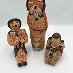 Puede incluir: Tres figuras de cerámica nativas americanas hechas a mano. Las figuras están pintadas en tonos tierra con detalles en negro. Una figura sostiene una cesta, otra sostiene varios niños y la tercera figura tiene un niño en su vientre.