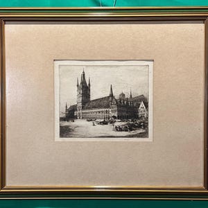 Op de afbeelding: Een antieke ingelijste prent van een gedetailleerde architectuurtekening. De zwart-wit ets toont een groot gebouw met meerdere torens en een plein. De lijst is goudkleurig met een groene buitenrand, op een beige passe-partout.