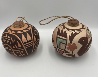 Peut inclure: Deux ornements ronds décoratifs avec des motifs peints à la main. L'un présente des motifs géométriques bruns et beiges, l'autre un oiseau, une fleur et des formes géométriques brunes, beiges et turquoise. Chacun a un bouchon marron et une boucle en ficelle.