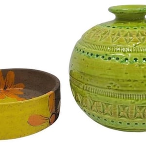 Op de afbeelding: Twee keramische stukken: een gele asbak met oranje bloemdetails en een groene, patroonvaas. De asbak heeft een bruin interieur en een gebogen vorm. De vaas is rond met een kleine hals en reliëfpatronen.