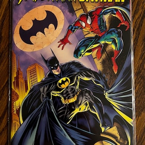 May include: Comic book cover featuring Spider-Man and Batman. The title "Spider-Man and Batman" is in yellow. Batman is in the foreground, and Spider-Man is in the background. The background is a cityscape with a purple sky.