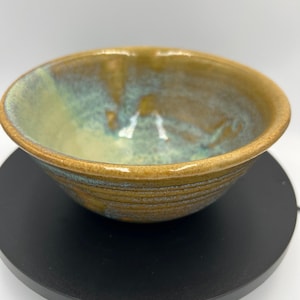 May include: A handcrafted ceramic bowl with a textured exterior and a glazed interior. The bowl features a blend of earthy tones, including brown, green, and blue, creating a unique aesthetic. The bowl is suitable for serving food.