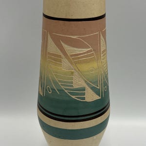 May include: A tall, decorative vase with a beige base and a cylindrical body. The vase features horizontal bands of color, including beige, pink, and teal, with etched geometric designs. The vase is approximately 10 inches tall.