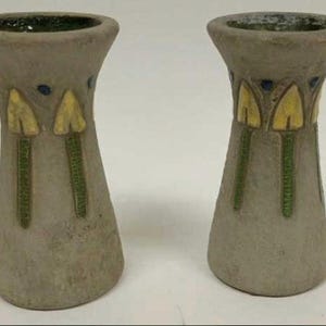 May include: Two gray ceramic vases with a flared shape. Each vase features yellow and green floral designs and a dark green interior. The vases are likely for decorative purposes.