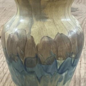 May include: A ceramic vase with a wide base and flared rim. The vase features a colour palette of beige, brown, and blue. The design includes brown tulip-like shapes over a blue and beige background. The vase is suitable for floral arrangements.