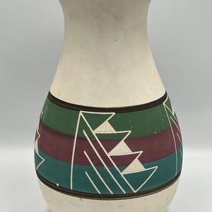Peut inclure: Vase en céramique crème avec une base large et un dessus évasé. Le vase présente une bande de rayures horizontales vertes, bordeaux et teal avec des motifs géométriques blancs. Une bande marron borde le haut et le bas du motif.
