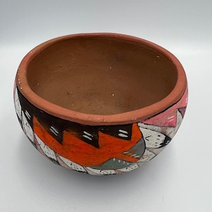 Könnte beinhalten: Handbemalte Terrakotta-Schale mit breitem Rand. Die Außenseite weist ein geometrisches Design in Orange-, Schwarz-, Weiß-, Rosa- und Grautönen auf. Der Innenraum ist einfarbig braun. Diese dekorative Schale ist für verschiedene Zwecke geeignet.