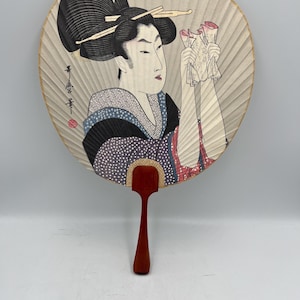 Könnte beinhalten: Japanischer Ukiyo-e-Fächer mit Holzgriff und Papierfläche. Der Fächer zeigt eine Frau in traditioneller Kleidung, die Papiere hält. Die Illustration ist detailliert und enthält japanischen Text. Ein traditionelles japanisches Objekt.