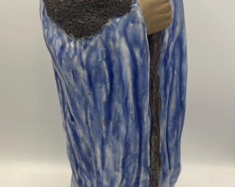 May include: A ceramic figurine of a wise man with a long beard, wearing a blue robe. The figure is holding a walking stick and has a serene expression. The statue is approximately 10 inches tall.