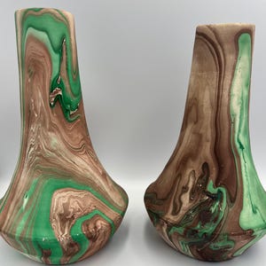 May include: Two decorative vases with a unique marbled design. The vases feature a blend of brown, green, and cream colors, creating a swirling pattern. The vases have a wide base and a flared top.