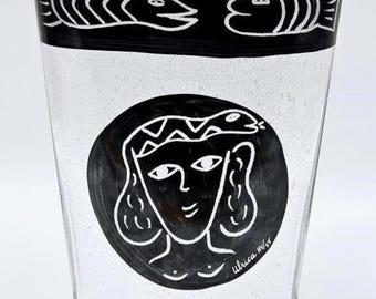 Könnte beinhalten: Klares Glas mit schwarz-weißen Illustrationen. Das obere Band zeigt zwei Fische, und ein zentrales kreisförmiges Design zeigt ein Frauengesicht. Die Signatur des Künstlers, "Ulrica M/55", ist sichtbar.