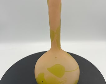 Könnte beinhalten: Eine Vase aus mattiertem Glas mit einem blass pfirsichfarbenen Grundton und matter Oberfläche. Die Vase hat einen schlanken Hals und einen bauchigen Körper, der mit einem sich wiederholenden Muster aus hellgrünen Blättern verziert ist.