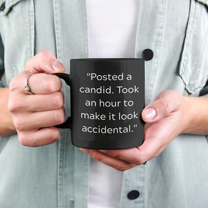 May include: Black coffee mug with white text that reads "Posted a candid. Took an hour to make it look accidental."
