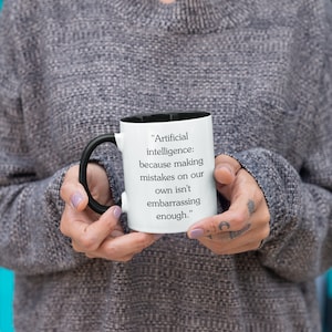 May include: White coffee mug with a black handle and black rim. The mug has a quote printed on it that reads "Artificial intelligence: because making mistakes on our own isn't embarrassing enough."