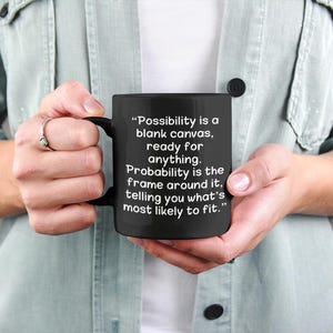 May include: A black coffee mug with a quote in white lettering: "Possibility is a blank canvas, ready for anything. Probability is the frame around it, telling you what's most likely to fit." The mug is held in both hands.