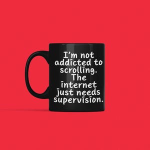 May include: A black ceramic mug with a handle on the left side. The mug features white text that reads: I'm not addicted to scrolling. The internet just needs supervision. The mug is set against a solid, bright red background.