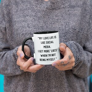 May include: White coffee mug with a black handle and black rim. The mug has a funny saying printed on it: "My love life is like social media. I get more 'likes' when I'm not being myself."