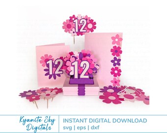 May include: A collection of pink and purple paper flower decorations with the number 12. Includes a cake topper, pop-up card, and floral embellishments. The design features layered paper flowers in various shades of pink and purple.