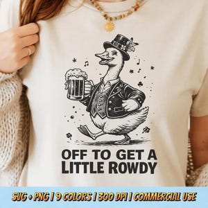 May include: Cream-colored t-shirt featuring a cartoon goose in a tuxedo holding a beer stein. The goose is walking with musical notes and shamrocks around it. The text "OFF TO GET A LITTLE ROWDY" is printed below the goose.