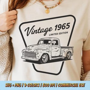 May include: A beige t-shirt with a black and white illustration of a classic pickup truck inside a black triangle. The text "Vintage 1965 Limited Edition" is above the truck. The shirt is being worn.