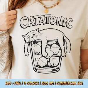 May include: Beige t-shirt with a black graphic of a cat lying in a glass of ice cubes, with the word "CATATONIC" above. The design is a humorous depiction of a cat in a relaxed state. The bottom of the image has text that reads "SVG + PNG | 9 COLORS | 300 DPI | COMMERCIAL USE".