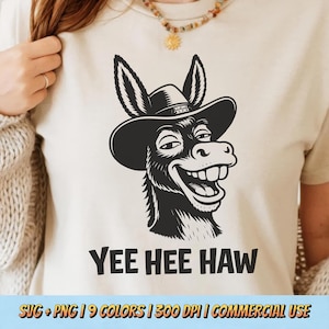 May include: A cream-colored t-shirt featuring a black and white illustration of a smiling donkey wearing a cowboy hat. The text "YEE HEE HAW" is printed below the donkey graphic. The shirt is a casual wear item.