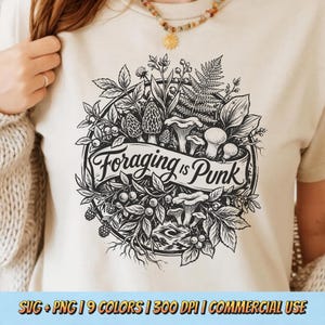 Puede incluir: Camiseta beige con una ilustración en blanco y negro de varias setas y follaje en un diseño circular. El texto "Foraging is Punk" se muestra en una pancarta. La camiseta la lleva una persona.