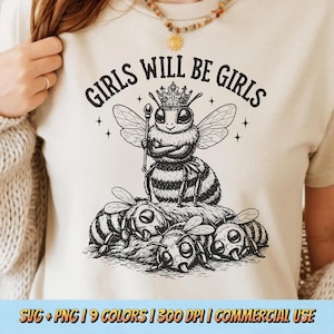 May include: A cream-colored t-shirt with the text "GIRLS WILL BE GIRLS" in black. The graphic features a queen bee wearing a crown and holding a scepter, surrounded by other bees. The bottom of the shirt has the text "SVG + PNG | 9 COLORS | 300 DPI | COMMERCIAL USE".