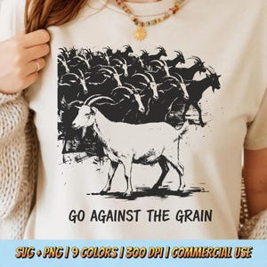 Puede incluir: Camiseta beige con una ilustración en blanco y negro de una cabra frente a una manada de cabras. El texto "GO AGAINST THE GRAIN" está debajo de la imagen. La camiseta tiene cuello redondo y mangas cortas.