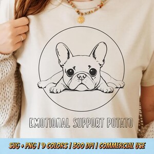 以下が含まれることがあります： クリーム色のTシャツ。黒と白のフレンチブルドッグのイラストが円の中に描かれています。「EMOTIONAL SUPPORT POTATO」の文字が下にあります。カジュアルなスタイルのシャツです。