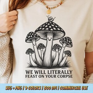 May include: Beige t-shirt featuring a black and white illustration of cartoon mushrooms with smiling faces and a snail. The text reads "WE WILL LITERALLY FEAST ON YOUR CORPSE".