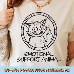 May include: Cream-coloured t-shirt with a black and white cat illustration giving the middle finger, within a dotted circle. The text "EMOTIONAL SUPPORT ANIMAL" is printed below the cat image.