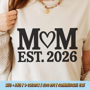 May include: Cream-colored t-shirt with the word "MOM" in bold black letters, a heart replacing the "O", and "EST. 2026" below. The shirt is part of a collection of SVG and PNG files.