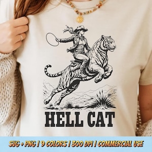 Könnte beinhalten: Beigefarbenes T-Shirt mit einer schwarz-weißen Grafik einer Cowgirl, die auf einem Tiger reitet und einen Lasso hält. Der Text "HELL CAT" steht unter dem Bild. Der untere Teil des Shirts hat den Text "SVG + PNG | 9 COLORS | 300 DPI | COMMERCIAL USE".