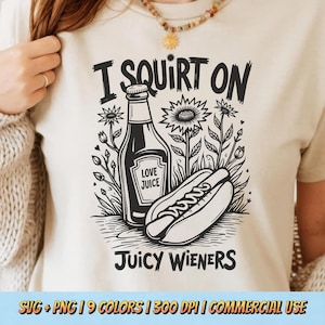 Op de afbeelding: Beige T-shirt met een zwart-witte afbeelding. De afbeelding toont een fles met het label "Love Juice" naast een hotdog, met de tekst "I SQUIRT ON" erboven en "Juicy Wieners" eronder. Bloemenelementen omringen het ontwerp.