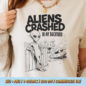 Puede incluir: Camiseta beige con un gráfico en blanco y negro de un extraterrestre apoyado en una valla de madera. El texto "ALIENS CRASHED IN MY BACKYARD" está encima de la ilustración del extraterrestre. Se muestran extraterrestres adicionales cerca de una barbacoa y un OVNI.