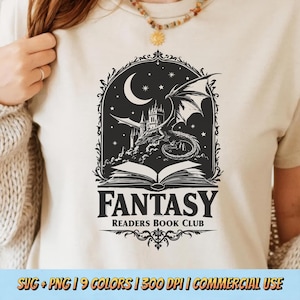 Op de afbeelding: Crèmekleurig T-shirt met een zwart-wit fantasieontwerp. Het ontwerp bevat een draak, kasteel en maan boven een open boek met de woorden "FANTASY" en "READERS BOOK CLUB" eronder gedrukt. Het shirt heeft een ronde hals.