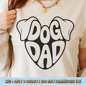 May include: A cream-colored t-shirt featuring a black and white graphic of the words "DOG DAD" in a heart-shaped design with dog ears. The bottom of the image includes text: SVG + PNG | 9 COLORS | 300 DPI | COMMERCIAL USE.