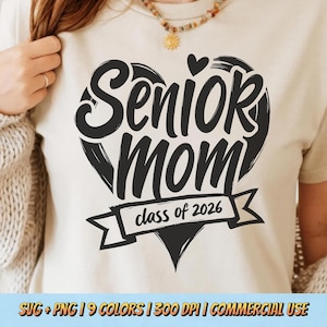 May include: Cream-colored t-shirt with a black heart-shaped design. The design features the words "Senior Mom" in a bold font, with "class of 2026" on a banner below. The shirt is a casual style.