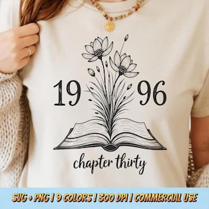 May include: Cream-colored t-shirt featuring a black floral design with the numbers "1996" and the words "chapter thirty." The design includes an open book with flowers and foliage sprouting from it. The shirt is a neutral color.