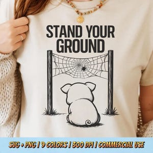 Könnte beinhalten: Ein cremefarbenes T-Shirt mit dem Text "STAND YOUR GROUND" über einer Grafik eines Schweins, das ein Spinnennetz betrachtet. Das Schwein sitzt vor einem Spinnennetz mit einer Spinne in der Mitte. Der untere Teil des Shirts hat den Text "SVG + PNG | 9 COLORS | 300 DPI | COMMERCIAL USE".
