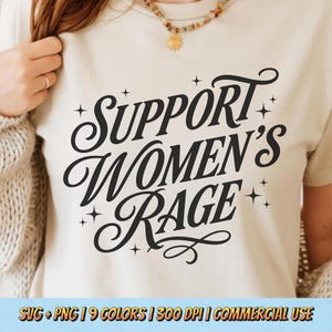 May include: A beige t-shirt with the words "SUPPORT WOMEN'S RAGE" in a bold, black, cursive font. The text is surrounded by small star shapes. The shirt is a neutral color and has short sleeves.