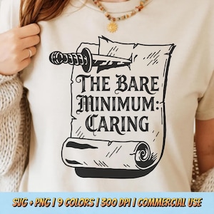 May include: A beige t-shirt displays a black graphic of a scroll with a sword through it, and the words "THE BARE MINIMUM: CARING." The scroll design has rolled edges and lines. The shirt is a neutral colour.